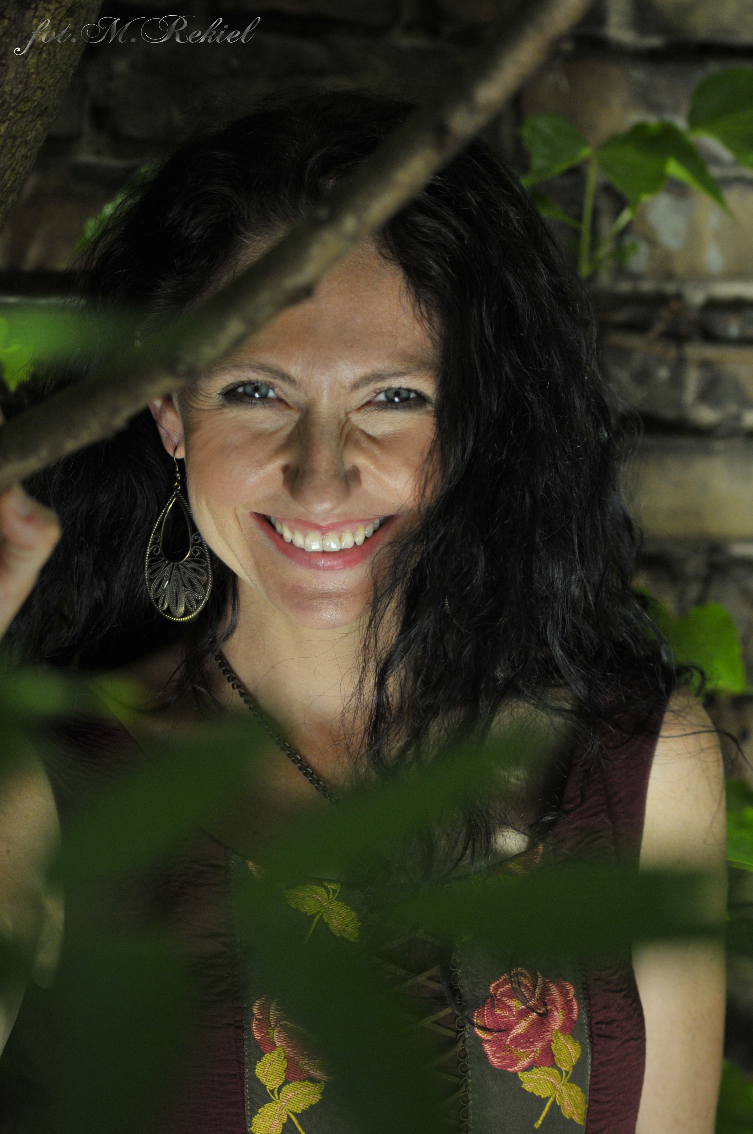 Portret uśmiechającej się kobiety (Anny Winiarskiej) skrytej wśród gałęzi i liści
